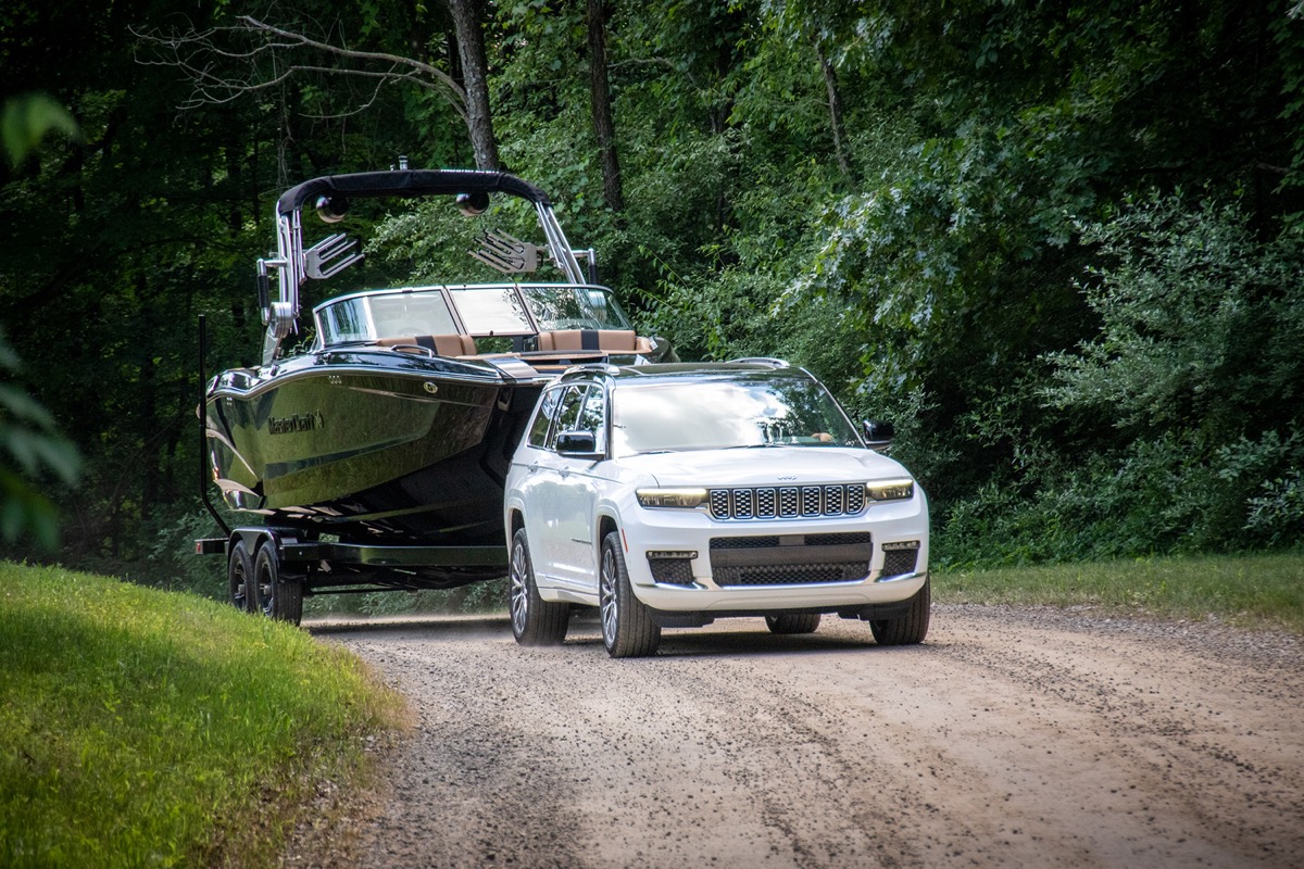 Le Jeep Grand Cherokee L 2021 blanc remorquant un bateau sur un chemin de terre en forêt